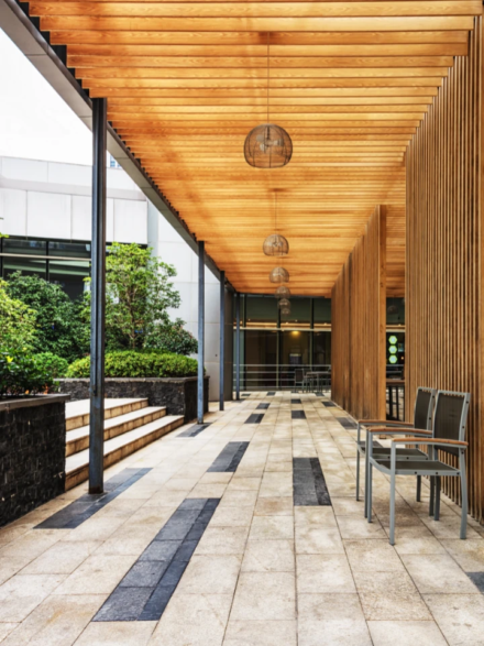 Couloir extérieur avec plafond en bois, sol carrelé à motifs, chaises modernes et végétation luxuriante.
