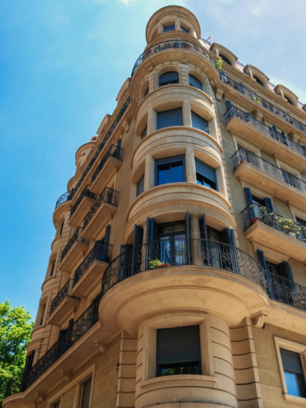 Immeuble haussmannien en pierre claire, aux balcons ferronnés et fenêtres cintrées, sous un ciel bleu éclatant.