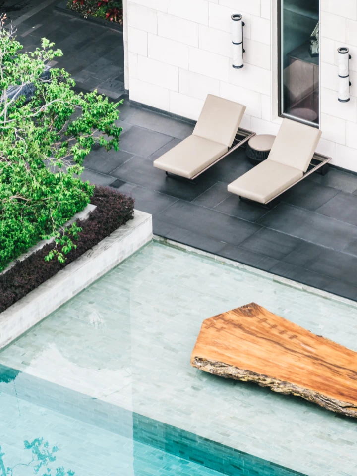 Piscine moderne avec transats, dalle de bois flottant et végétation luxuriante, dans un cadre architectural épuré et lumineux.